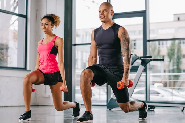 Cheerful couple of athletes doing exercise with dumbbells at gym — Stock Photo