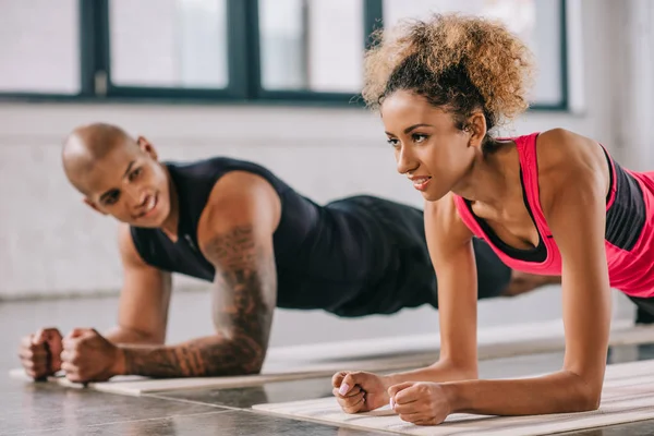 Attraktive afrikanisch-amerikanische Sportlerin beim Planken mit ihrem Freund im Fitnessstudio — Stock Photo