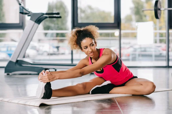 Cheerful african american sportswoman stretching on fitness at gym — Stock Photo