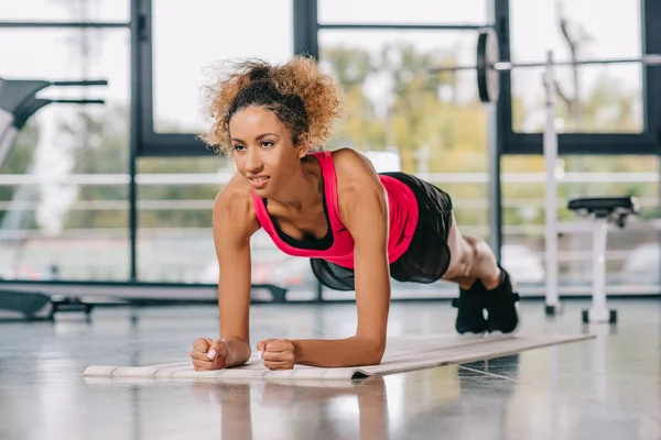 Heureuse sportive afro-américaine faisant planche sur tapis de fitness à la salle de gym — Photo de stock