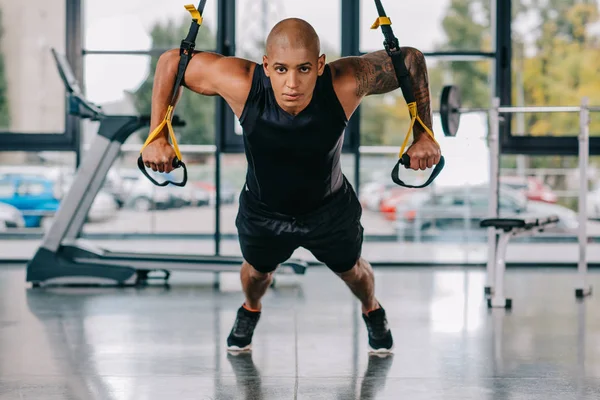 Deportista afroamericano mirando a la cámara y ejercitándose en correas de fitness en el gimnasio — Stock Photo