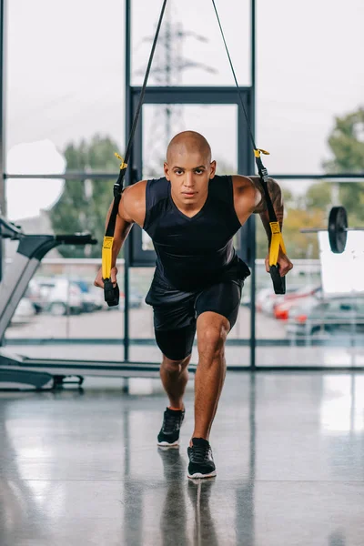 Focalizzato sportivo afro-americano che si esercita sulle cinghie fitness in palestra — Foto stock