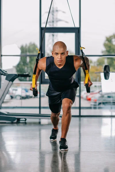 Sportif afro-américain concentré faisant de l'exercice sur les sangles de fitness au gymnase — Photo de stock