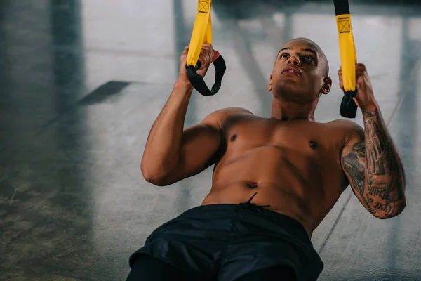 Deportista afroamericano concentrado ejercitándose en correas de suspensión en el gimnasio - foto de stock
