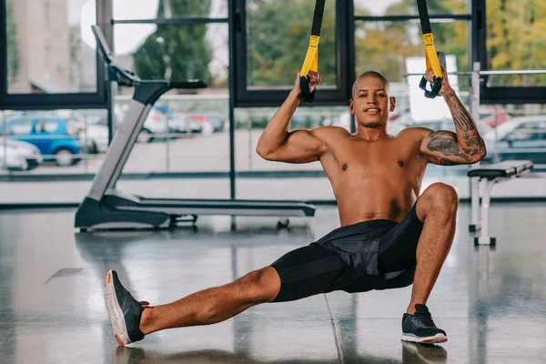 Веселый африканский американский спортсмен, тренирующийся на ремнях подвески в спортзале — стоковое фото