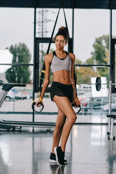 Afrikanisch-amerikanische Sportlerin schaut weg und posiert in der Nähe von Federbeinen im Fitnessstudio — Stockfoto