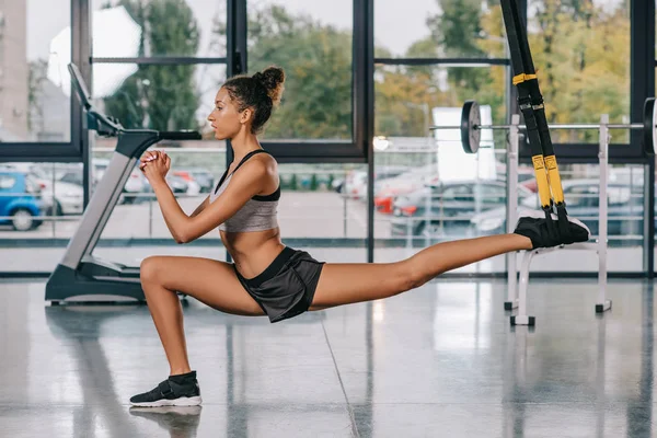 Seitenansicht einer afrikanisch-amerikanischen Sportlerin, die sich im Fitnessstudio auf Fitnessbändern dehnt — Stockfoto