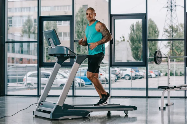 Enfoque selectivo del deportista afroamericano corriendo en la cinta de correr en el gimnasio - foto de stock