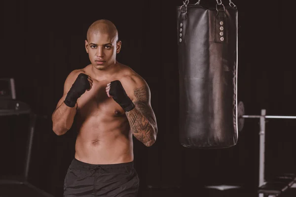 Schwerer afrikanisch-amerikanischer Boxer posiert in Kampfposition neben Boxsack im Fitnessstudio — Stockfoto