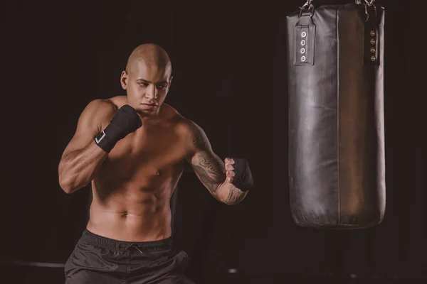 Entrenamiento de boxeador masculino afroamericano muscular con saco de boxeo en el gimnasio - foto de stock