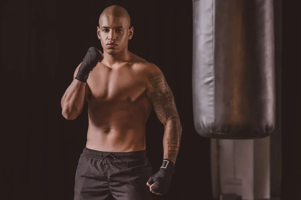 Selbstbewusster afrikanisch-amerikanischer Boxer posiert in Turnhalle in der Nähe eines Boxsacks — Stockfoto