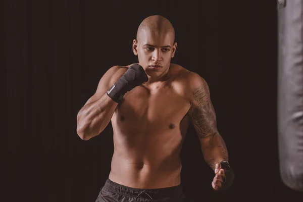 Boxeador masculino en entrenamiento de vendas de boxeo con saco de boxeo en el gimnasio - foto de stock