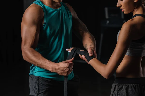 Imagem recortada de treinador masculino com mão tatuada embrulhando mão boxeador feminino em bandagem de boxe no ginásio — Fotografia de Stock