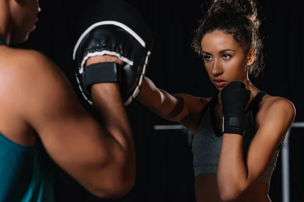 Vista parcial del entrenador personal masculino haciendo ejercicio con boxeadora femenina en el gimnasio — Stock Photo