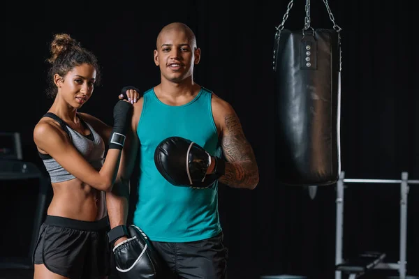 Enfoque selectivo de par afroamericano de boxeadores de pie cerca de saco de boxeo en el gimnasio - foto de stock