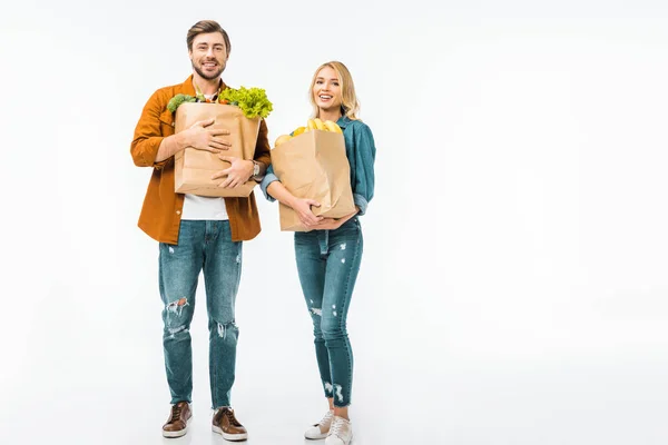 Jeune couple positif avec des sacs en papier plein de produits isolés sur blanc — Photo de stock