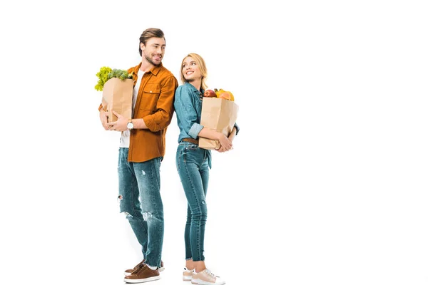 Casal com sacos de compras cheios de produtos olhando um para o outro e de pé para trás isolado no branco — Fotografia de Stock