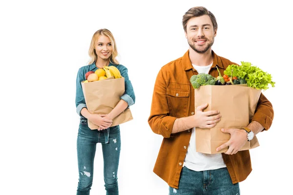 Felice giovane uomo in possesso di shopping bag con prodotti mentre la sua ragazza in piedi dietro isolato su bianco — Foto stock