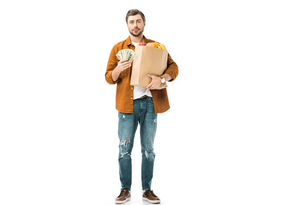 Young man showing cash money and holding paper bag full of products isolated on white — Stock Photo