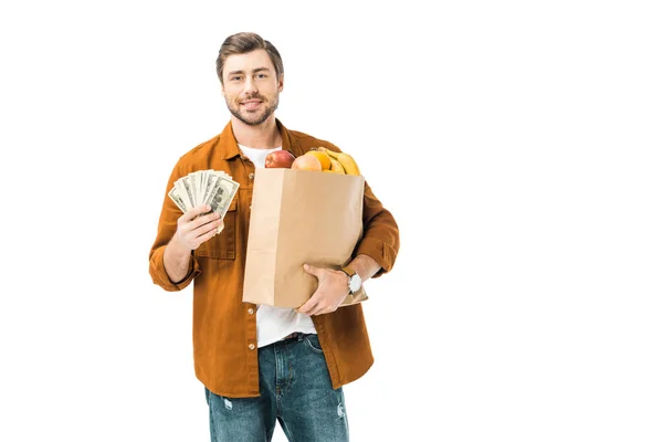 Glücklicher Mann zeigt Bargeld und hält Papiertüte voller Produkte isoliert auf weiß — Stock Photo