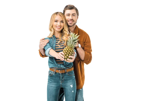 Sonriente hombre abrazando novia mientras ella mostrando piña aislado en blanco - foto de stock