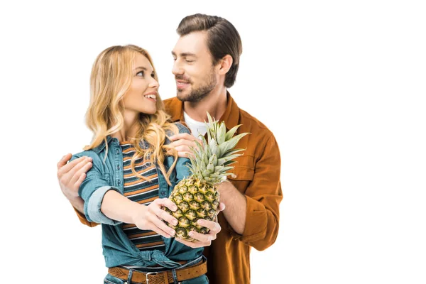 Handsome man embracing girlfriend while she showing pineapple isolated on white — Stock Photo