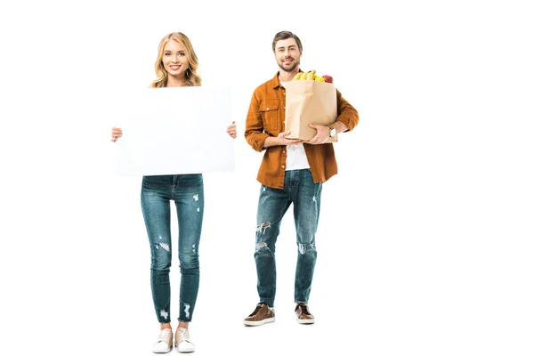 Joven mujer mostrando pancarta en blanco mientras su novio de pie con productos en bolsa de papel - foto de stock