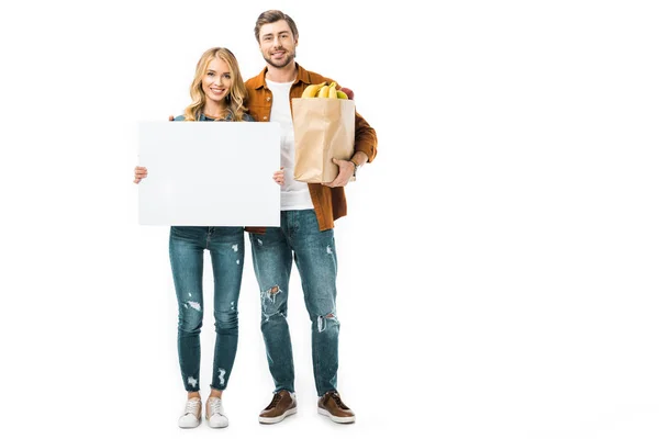 Bonita mujer mostrando banner en blanco mientras su novio de pie con productos en bolsa de papel - foto de stock