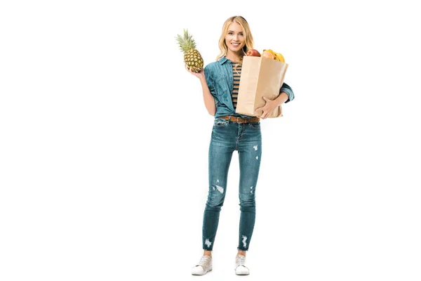 Mujer joven sosteniendo piña y bolsa de papel con productos aislados en blanco - foto de stock