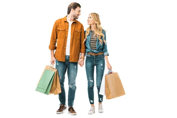 Pareja joven mirándose unos a otros y sosteniendo coloridas bolsas de papel aisladas en blanco - foto de stock