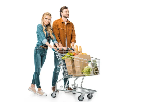 Fröhliches Paar trägt Einkaufswagen mit Produkten auf weißem Grund — Stockfoto