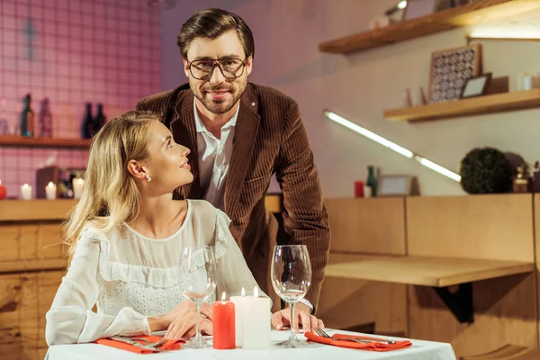 Fröhlicher Mann in Jacke umarmt Freundin am Tisch mit Kerzen im Café — Stockfoto