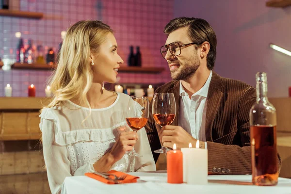 Sonriente pareja tintineando por copas de vino en la mesa con velas en el restaurante - foto de stock