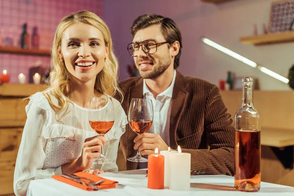 Pareja riendo con copas de vino celebrando y teniendo cita en la mesa con velas en el restaurante - foto de stock