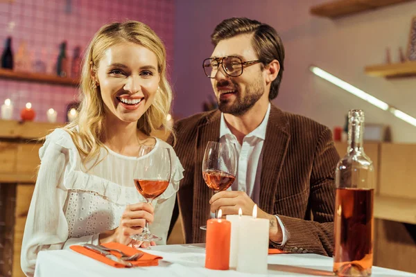 Couple heureux avec des verres à vin célébrant et ayant rendez-vous à table avec des bougies au restaurant — Photo de stock