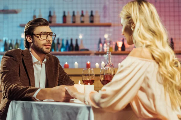 Focalizzazione selettiva di coppia che si tiene per mano e cena romantica a tavola con candele e bicchieri di vino nel ristorante — Foto stock
