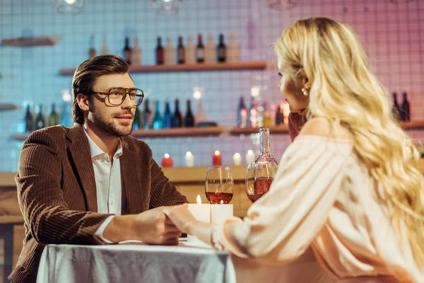 Junges lächelndes Paar Händchen haltend und romantisches Abendessen am Tisch mit Kerzen und Weingläsern im Restaurant — Stockfoto