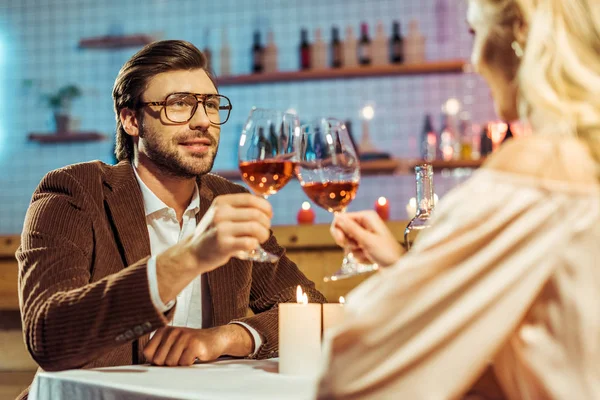 Foco seletivo de jovem casal celebrando e clinking por copos de vinho à mesa com velas no restaurante — Fotografia de Stock