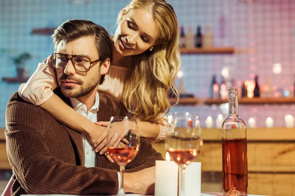Hermosa joven abrazando novio molesto durante la cena romántica en la mesa en el restaurante - foto de stock