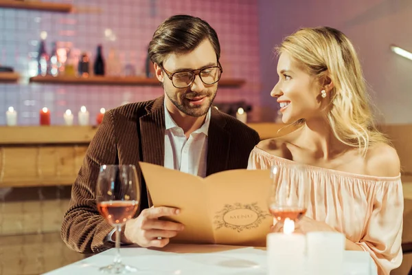 Feliz pareja joven mirando el menú durante la cena romántica en el restaurante - foto de stock