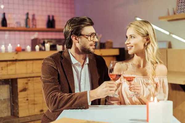 Alegre pareja tintineo por copas de vino durante la fecha en la mesa en la cafetería - foto de stock