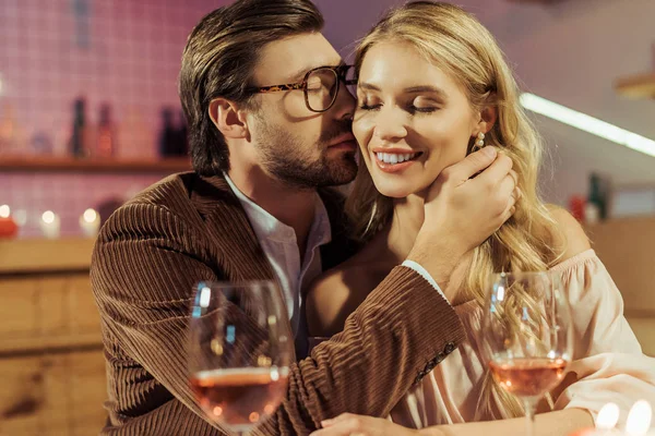 Vue latérale du jeune homme en veste embrasser belle petite amie pendant le dîner romantique au restaurant — Photo de stock