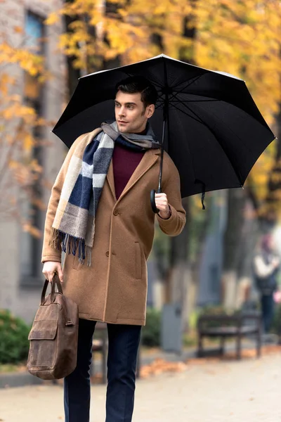 Attraente uomo elegante in cappotto con ombrello a piedi da strada autunnale — Foto stock