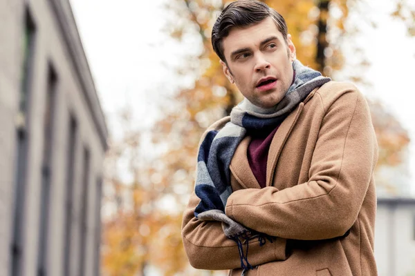 Vista inferior del hombre guapo en abrigo congelándose en la calle otoñal - foto de stock