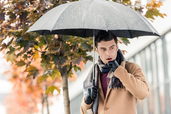 Handsome stylish man with umbrella standing on autumnal street — Stock Photo