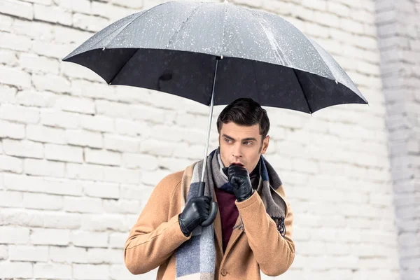 Homem elegante em casaco e cachecol com guarda-chuva de pé na frente da parede de tijolo na rua — Fotografia de Stock