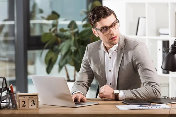 Bel homme d'affaires confiant assis sur le lieu de travail et regardant loin dans le bureau moderne — Photo de stock