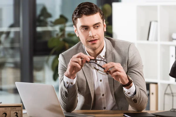 Handsome successful businessman sitting at workplace in office and looking away — Stock Photo