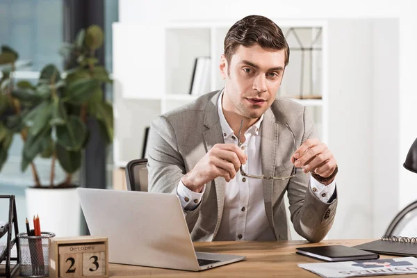 Guapo hombre de negocios con anteojos mirando a la cámara en la oficina - foto de stock