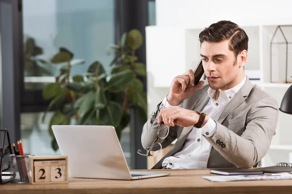 Handsome confident businessman talking by phone at workplace in office — Stock Photo